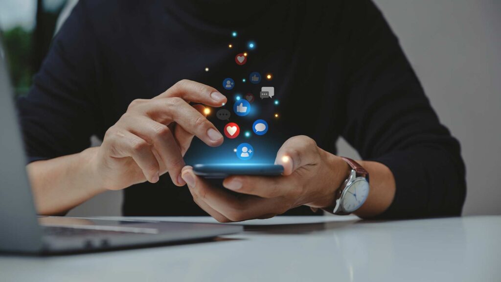 Professional social media marketing - A person's hands using a smartphone, with various social media icons and engagement symbols floating around the device, suggesting the use of digital tools and platforms for effective social media marketing.